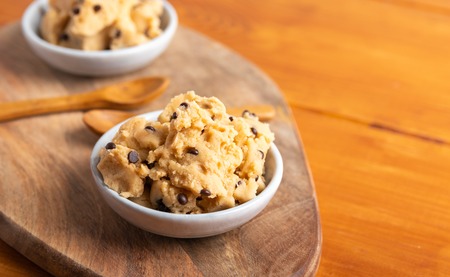 A serving of homemade cookie dough on a wooden table, with a wooden spoon.