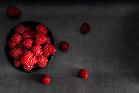 Fruit, red raspberry in a black bowl on a dark background with a bottle of juice on the side.の写真素材