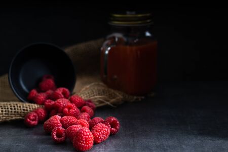 Fruit, red raspberry in a black bowl on a dark  with a bottle of juice on the side.