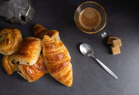 Breakfast with croissants, cinnamon buns and chocolate cookies, fresh orange juice and coffee on the side on a dark background in a spot light. Top view.の写真素材