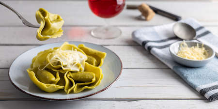 Homemade organic tortellini filled with spinach and cheese on a white table with a glass of wine on the side.の写真素材