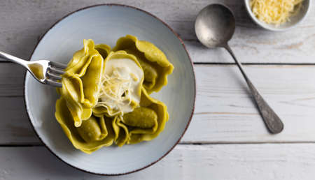 Homemade organic tortellini filled with spinach and cheese on a white table with a glass of wine on the side. Top view.の写真素材
