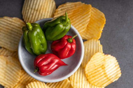 Homemade hot chips with jalapeno peppers on the side. On a dark colored table top. Top view.