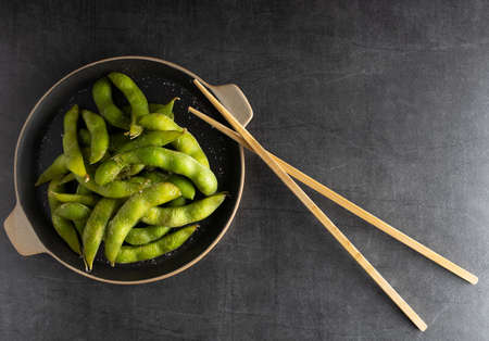 Japanese appetizer Edamame green soy beans seasoned with salt in a bowl, with shop sticks on the side.の写真素材