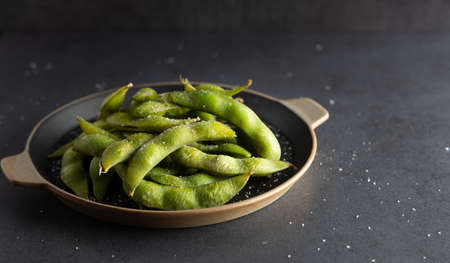 Japanese appetizer Edamame green soy beans seasoned with salt in a bowl, with shop sticks on the side.の写真素材