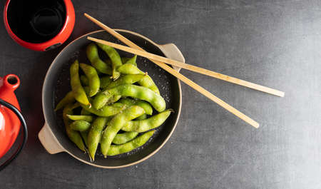 Japanese appetizer Edamame green soy beans seasoned with salt in a bowl, with shop sticks on the side.の写真素材