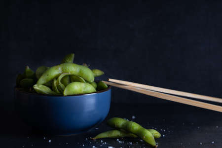 Japanese appetizer Edamame green soy beans seasoned with salt in a bowl, with shop sticks on the side.の写真素材