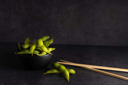 Japanese appetizer Edamame green soy beans seasoned with salt in a bowl, with shop sticks on the side.の写真素材