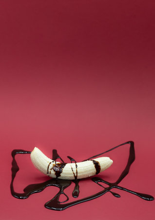 Peeled banana in one piece with chocolate sauce garnished on red background with copy spaceの写真素材