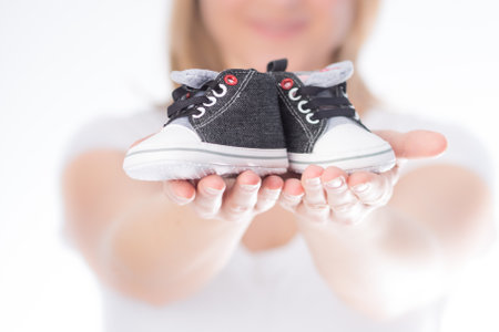 Woman holds a pair of children's shoes in her hands with white background. horizontal