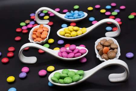 tryspoon for party buffet or birthday with sweets, smarties in different colors on black background. horizontalの写真素材