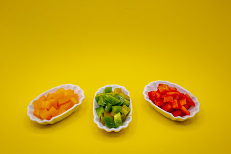 Small bowls with healthy red, green, and red peppers cut into cubes. horizontal with yellow backgroundの写真素材