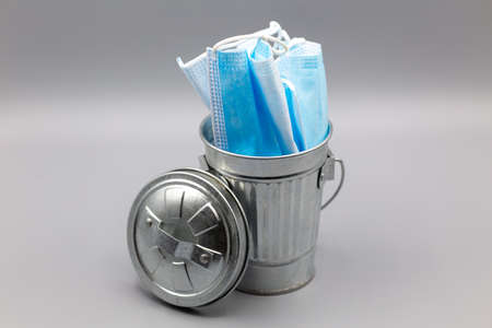 times with blue medical masks in the garbage bin on grey backgroundの写真素材