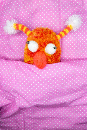 Cuddly orange toy for children in bed under a pink duvet with white dots for congratulations or greeting cardの写真素材