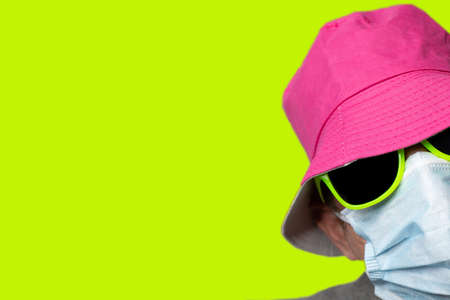 Man with pink hat yellow sunglasses and medical mask and yellow backgroundの写真素材