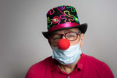 Man with medical mask, clown nose and depressed facial expression at carnival