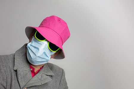 Male person with face mask, sunglasses and pink hat on neutral grey background.の写真素材