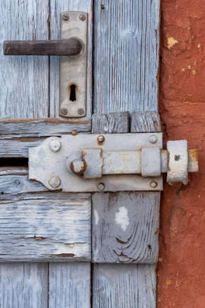Old used wooden door with closed and bar on red house facade, very used with weather traces in vertical format. Architectureの写真素材
