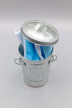 Garbage can filled with blue disposable medical masks during   pandemic on gray background. Verticalの写真素材