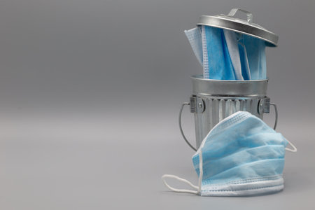 Medical masks in and around garbage can with lid d  on gray background. Horizontalの写真素材