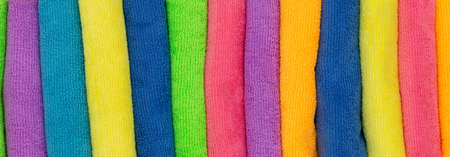 Towels and cleaning cloths in various colors as background to the topics shower, household and hygiene with the colors pink, yellow and blue. Horizontal wideの写真素材