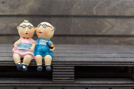 Plastic figures of an old, in love couple sits contentedly, healthy and in a good mood on a brown bench or wooden pallet and talk. Horizontalの写真素材