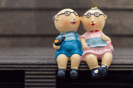 Plastic figures of an old senior couple in love sits contentedly, healthy and in a good mood on a bench or wooden pallet and talk happy together. Horizontalの写真素材