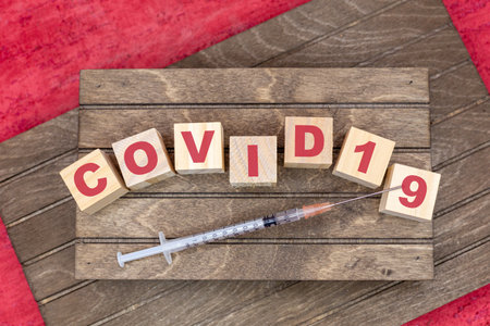 Word covid19 with letters on wooden cubes and wood background with red color and inject for Covid-19 vaccination in the vaccination center or at family doctors. Horizontalの写真素材