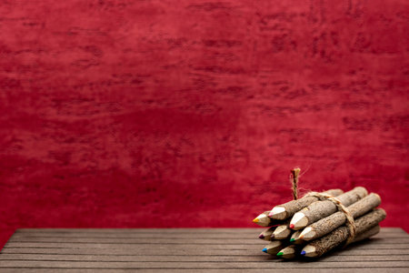 bound crayons made of real, untreated wood with real tree bark on wooden board and red background for students and artists with copy space. Horizontalの写真素材