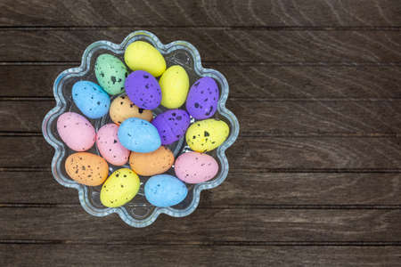 Glass bowl with many colorful Easter eggs taken from top with dark wooden background to Easter and...