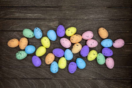 many colorful Easter eggs made of plastic lie at Easter on a rustic wooden board in color blue,...