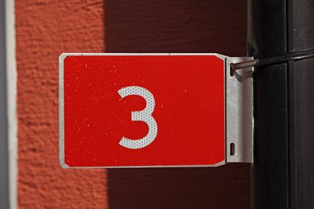 the number three on a red sign with reflective white text mounted on a downpipe at Umedalenの写真素材