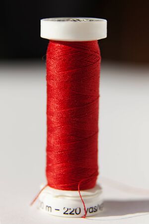red sewing thread wrapped on a white plastic roll in studio light