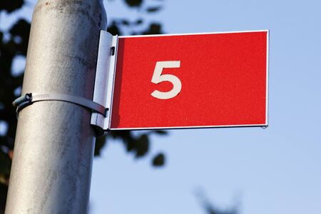 red sign with white text outdoors with the number five, a small drop of water at the bottom of the...