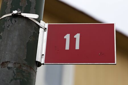 the digit eleven on a red metal sign with white text, the sign is stuck on a green rusty lamp postの写真素材