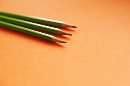 three green pencils lying on an orange backgroundの写真素材
