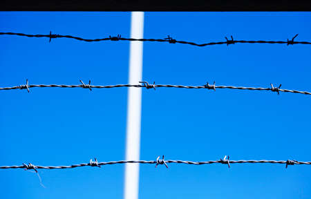 Three lines of barbed wire against a blue skyの写真素材
