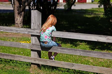 Umea, Norrland Sweden - June 24, 2020: little girl with red hair sits on a fence and is boredのeditorial素材