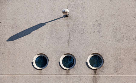 concrete wall with three round windows and with a lamp above