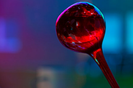 A striking macro photograph captures a single red water droplet suspended against a blurred blue background, creating a mesmerizing interplay of color, light, and reflection.の写真素材