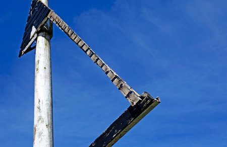 A weathered triangular metal structure mounted on a white pole stands starkly against a vibrant blue sky, creating a geometric silhouette with strong contrast and minimalist composition.の写真素材