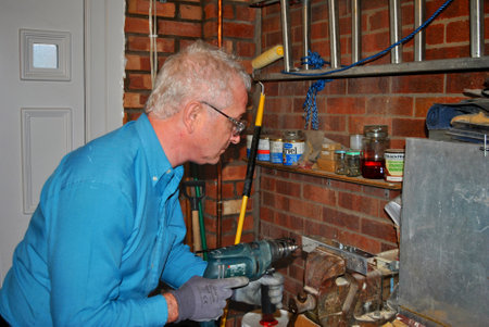 Man drilling a hole inside a garage wearing safety glasses and glovesのeditorial素材