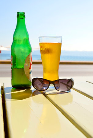 Ipsos, Corfu, Greece - October 5, 2017 : Ipsos Beach bottle of beer with glass and sunglassesのeditorial素材