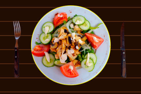 A plate of chicken and mushroom salad on a brown tableの写真素材