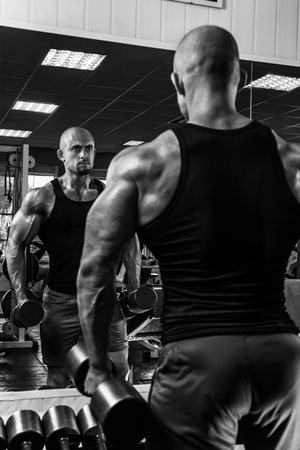 White Muscular man is posing in the gym with dumbbells and looking at mirror BWの写真素材
