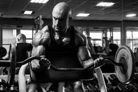 White Muscular man training his arms in the gym by barbell in the curl bench BWの写真素材
