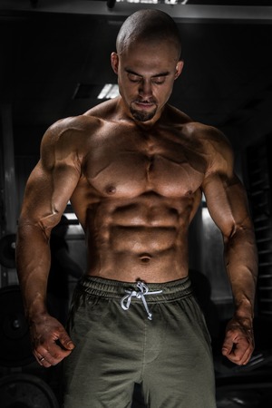 White Muscular man fitness model is posing in the gym and looking down