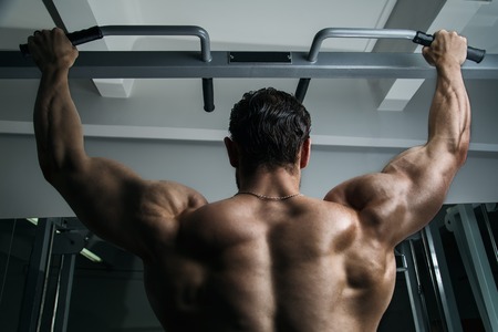 White Muscular man fitness model hanging on the chin-up bar, showing his back