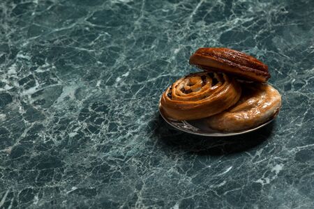 cinnamon bun, Bun with raisins, meat pie on saucer on green marble backgroundの写真素材