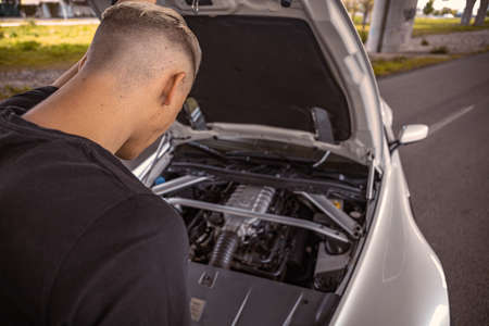 Young male taking a look at his car engine with the hood popped